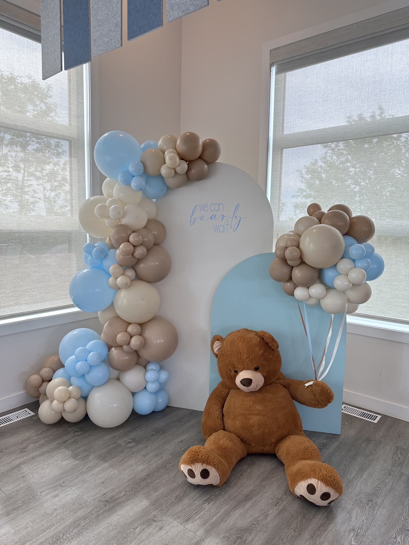 Blue, tan and cream balloon garland on arched backdrops with a large teddy bear at a Winnipeg baby shower