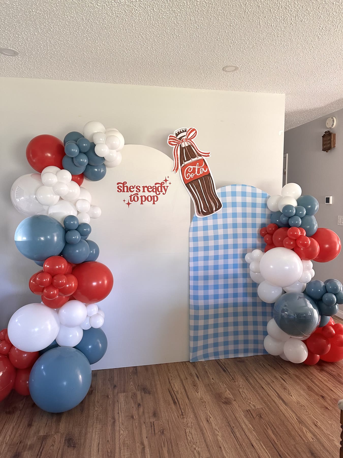 Red, blue and white balloon garland with a gingham panel and a She&rsquo;s Ready to Pop sign at a Winnipeg baby shower