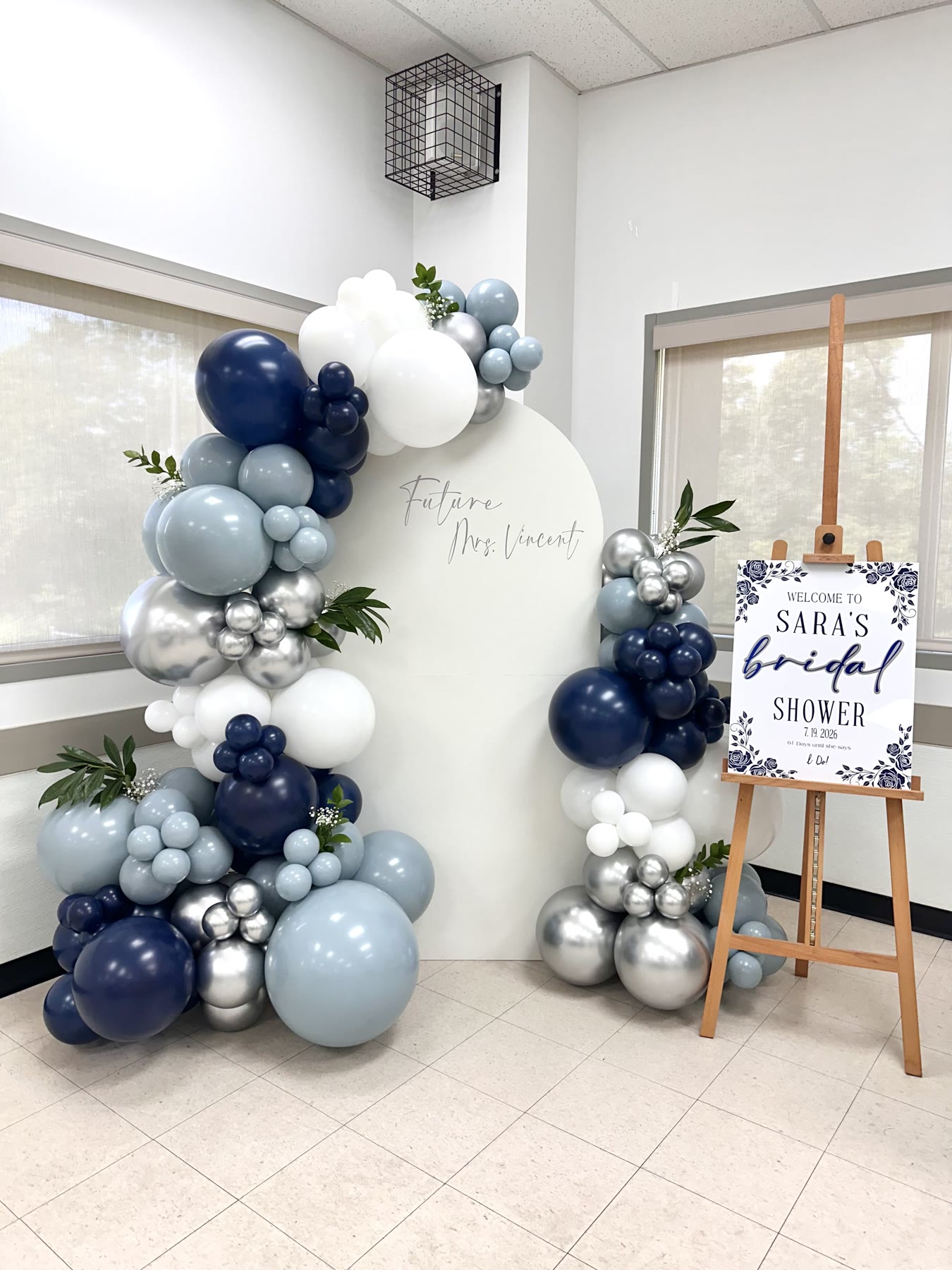 Navy and silver balloon garland with greenery on a white arched backdrop beside a bridal shower welcome sign, Winnipeg