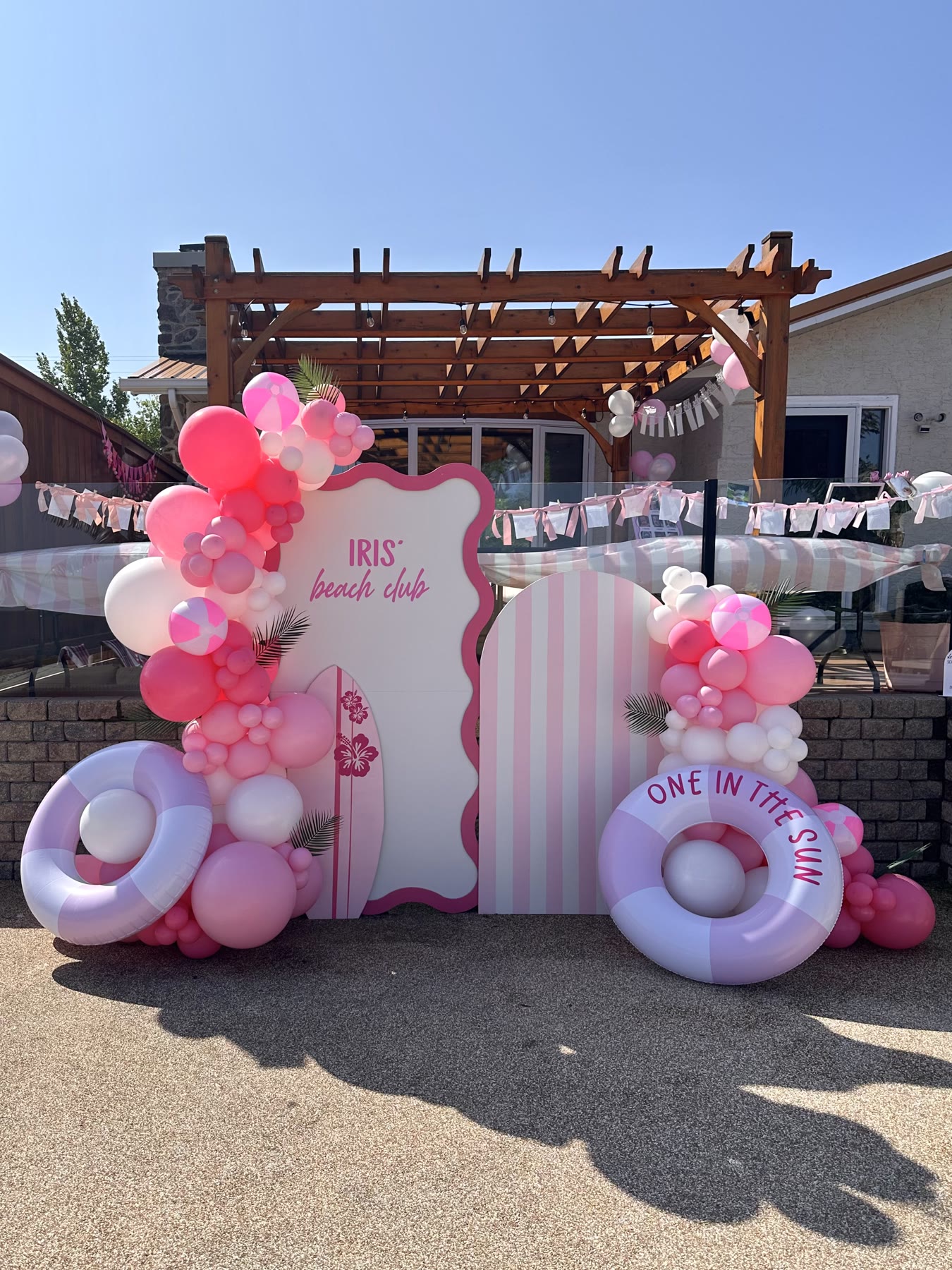 Pink and lilac balloon garland on arched backdrops with pool floats at an outdoor first birthday in Winnipeg